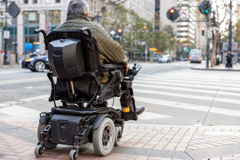 Older man in power wheel chairs waiting at a downtown crosswalk