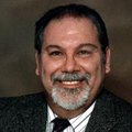 smiling light skinned man with dark short hair and gray beard in suit