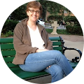 smiling light skinned woman with short brown hair and glasses sitting on a park bench
