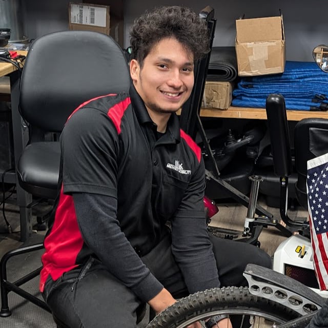 Field service technician Brian, a young, smiling man with dark curly hair working on a tire.