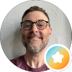 Smiling man with stubbled facila hair and glasses.